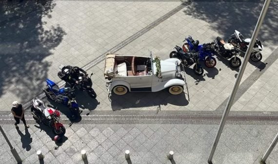 weisses brautcabriolet mit blumengirlande und motorrad eskorte